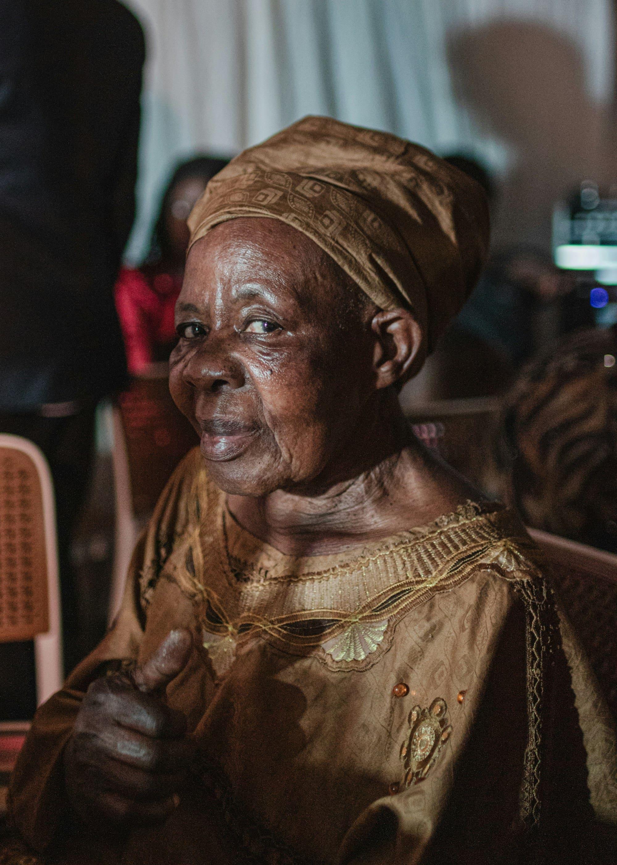 An older woman in a headwrap smiles warmly