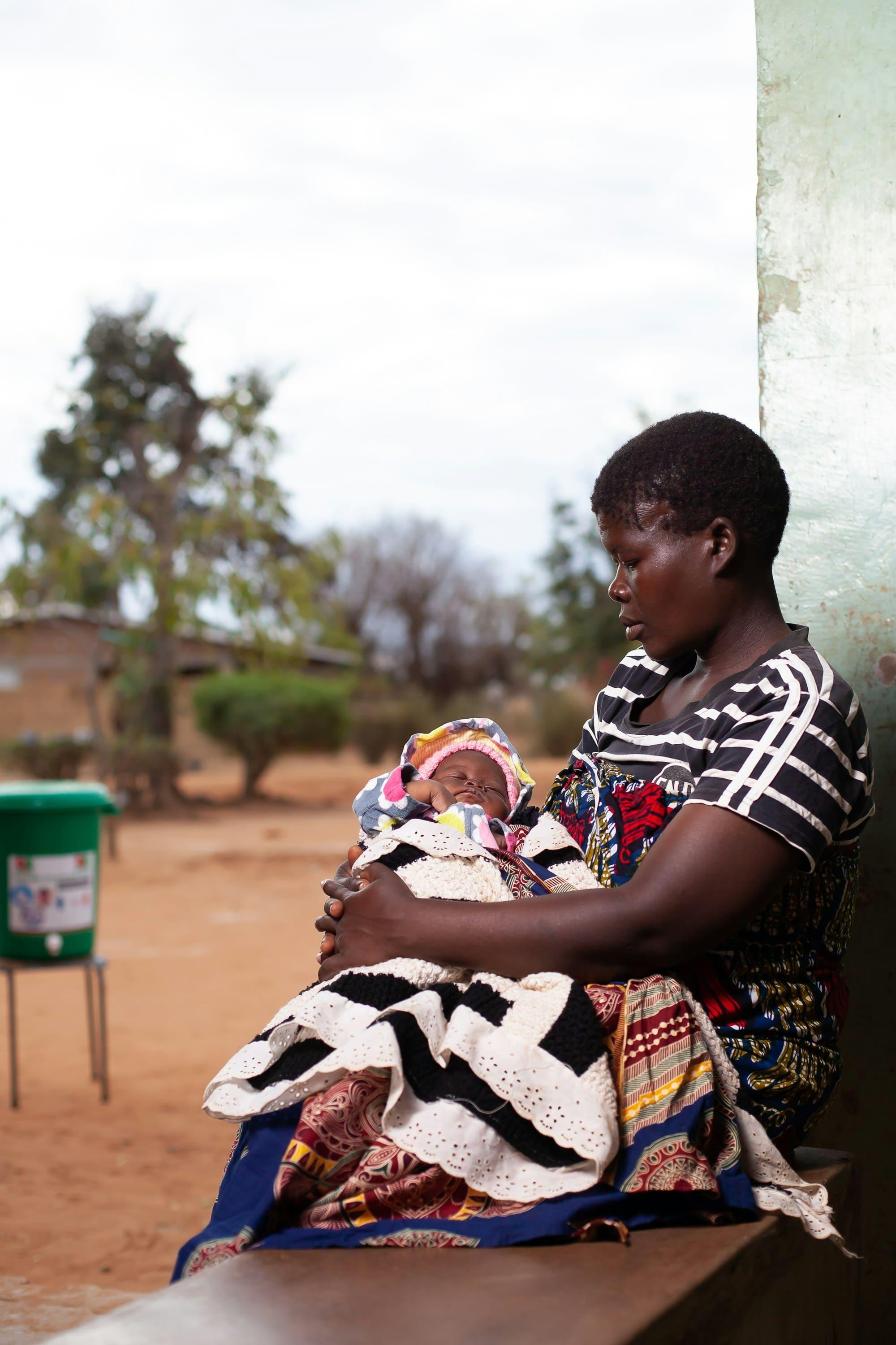 A mother holds her newborn baby wrapped in a patterned blanket